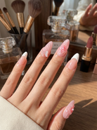 Hand with pink and white press on nails  in front of makeup items on a wooden surface
