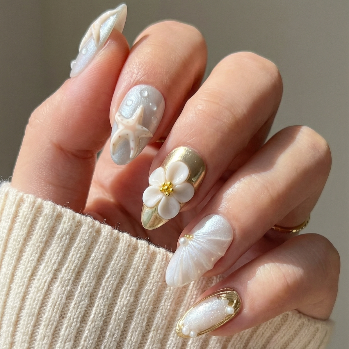 Hand with decorative nail art featuring flowers and gold accents against a neutral background