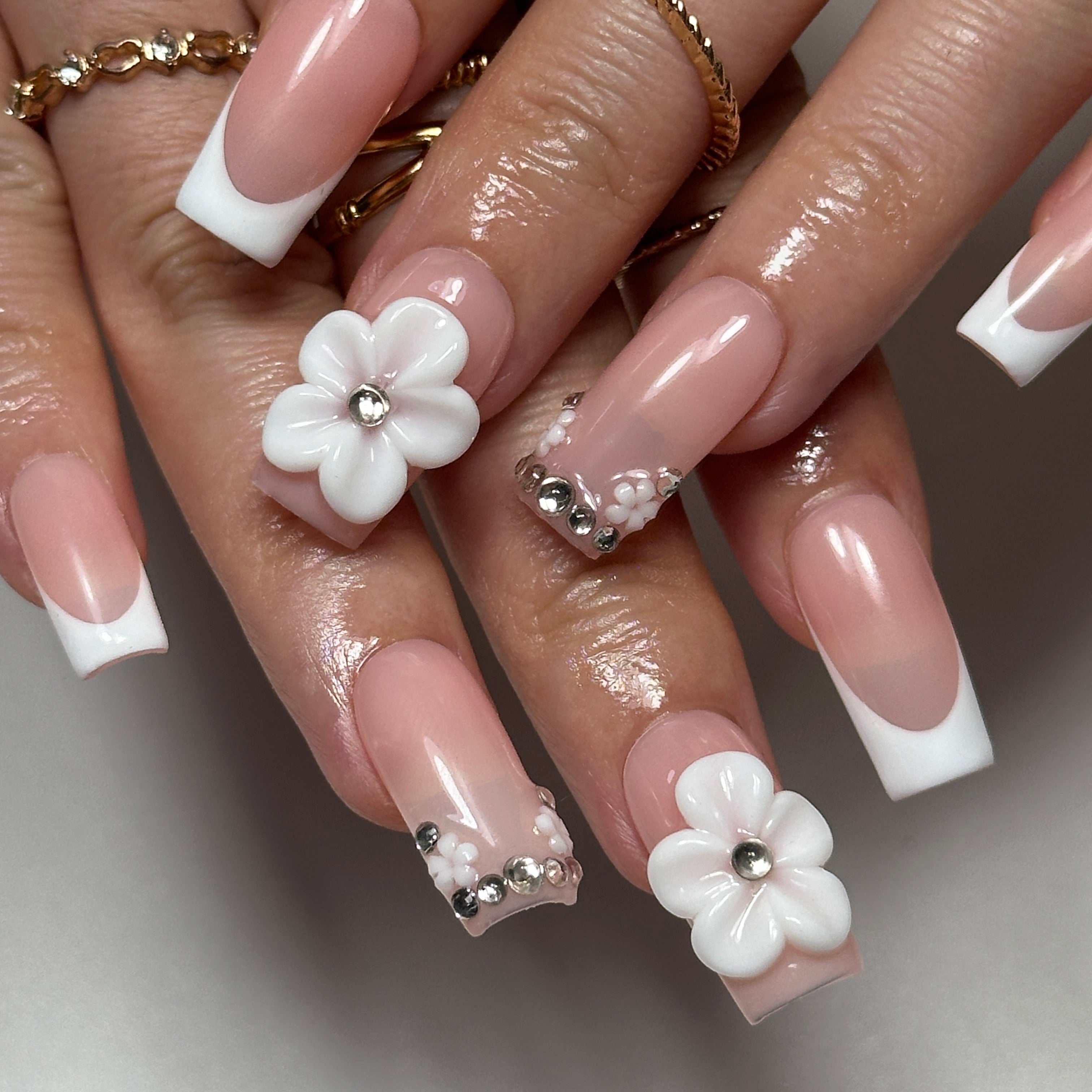 Close-up of hands with decorative nails featuring white flowers and silver accents.