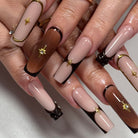 Close-up of hands with long, multicolored nails featuring gold star decorations on a neutral background.