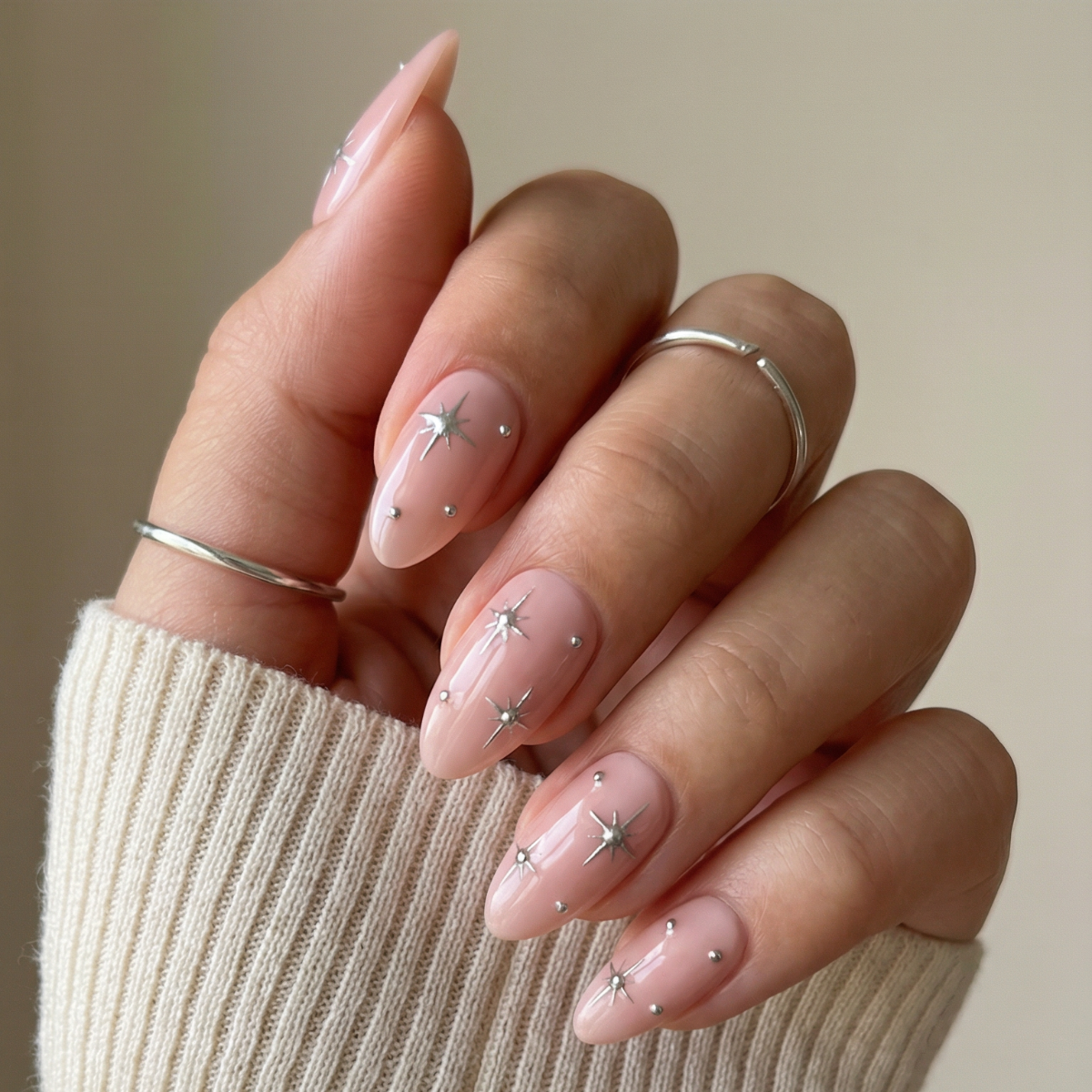 Hand with pink nails with star designs wearing a beige sweater, above a grid of nail color swatches.