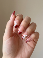 Hand with red and white nail design on a neutral background
