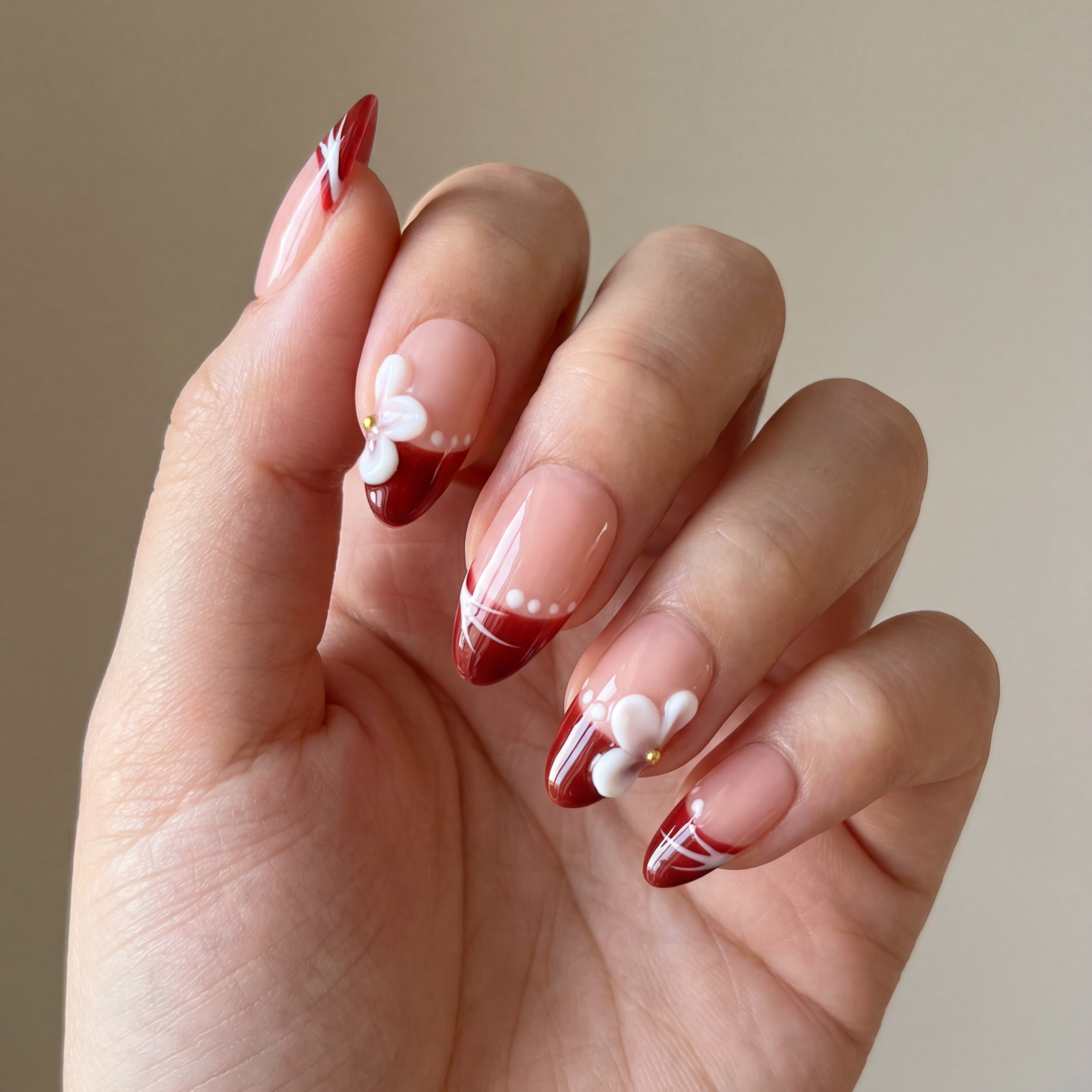 Hand with red and white nail design on a neutral background