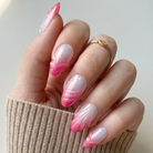 Hand with pink and white gradient nails wearing a beige sleeve.