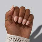 Hand with beige nail polish and gold accents on a neutral background