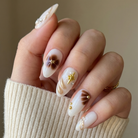 Hand with decorative nail art wearing a beige sweater against a neutral background